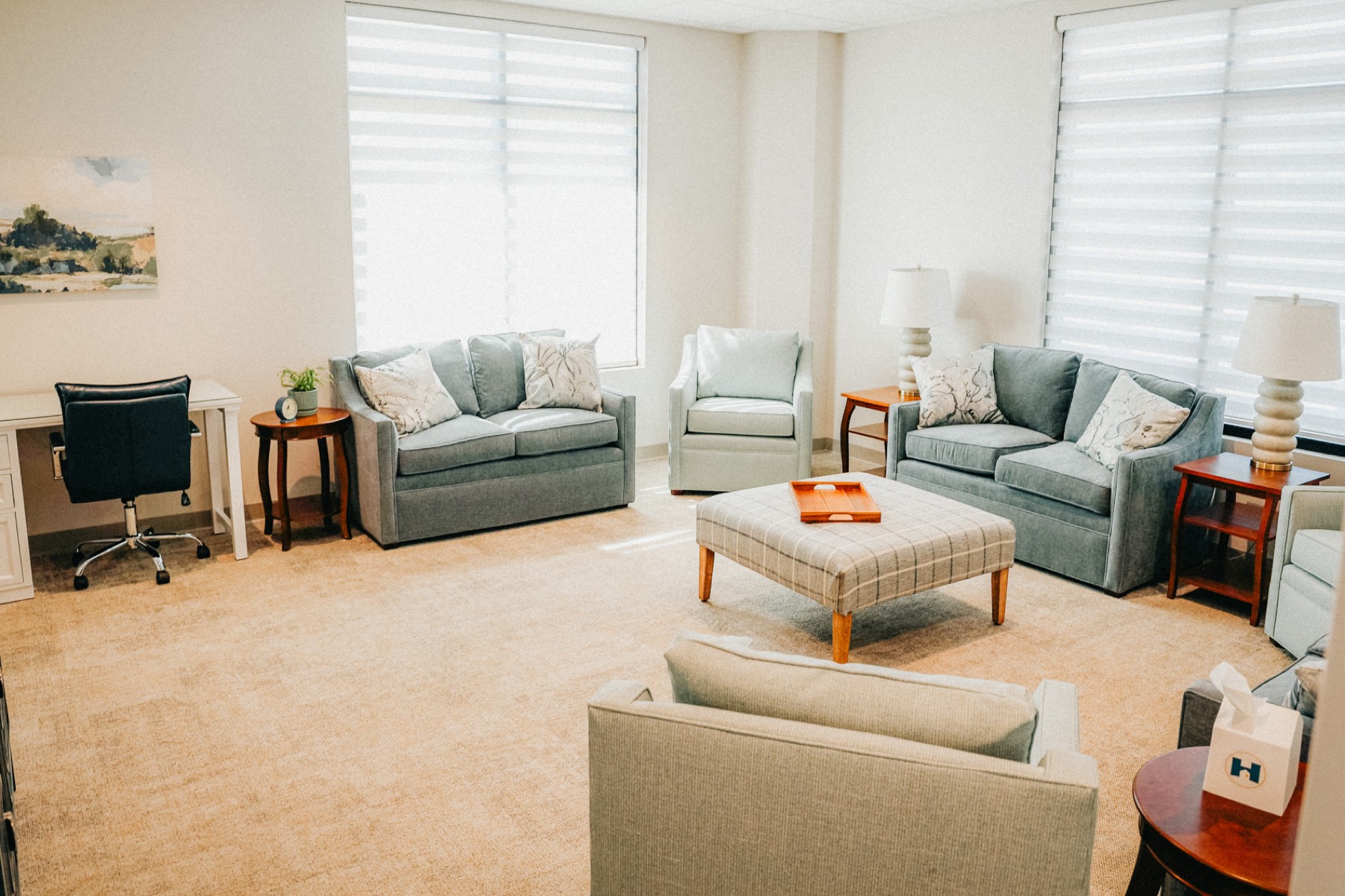 A bright counseling room with soft blue sofas and a wooden coffee table